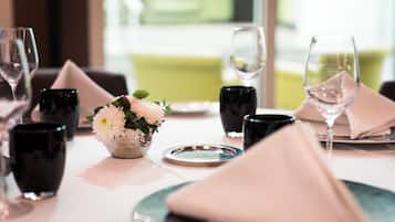 A dining table set with black glasses, a silver bowl with flowers, and a white plate.