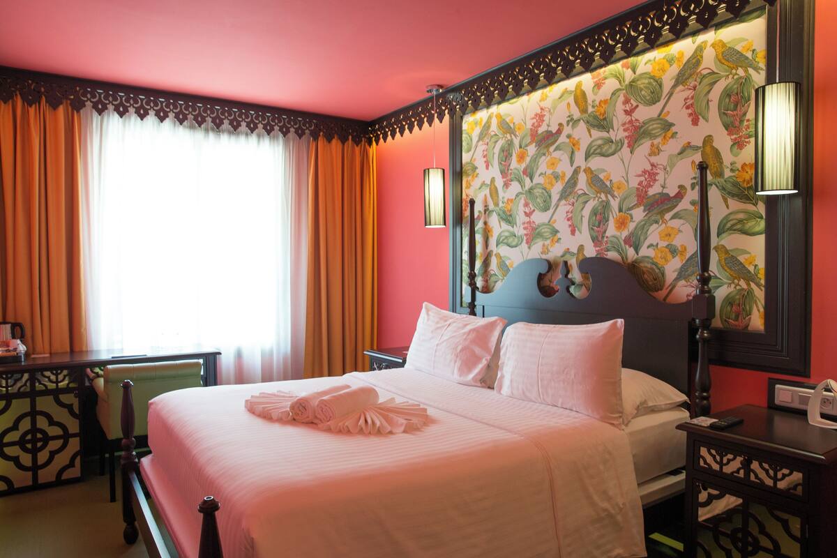 A hotel room with a large bed, a nightstand, a desk, and a window with curtains.