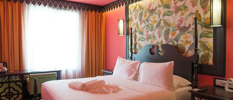 A hotel room with a large bed, a nightstand, a desk, and a window with curtains.