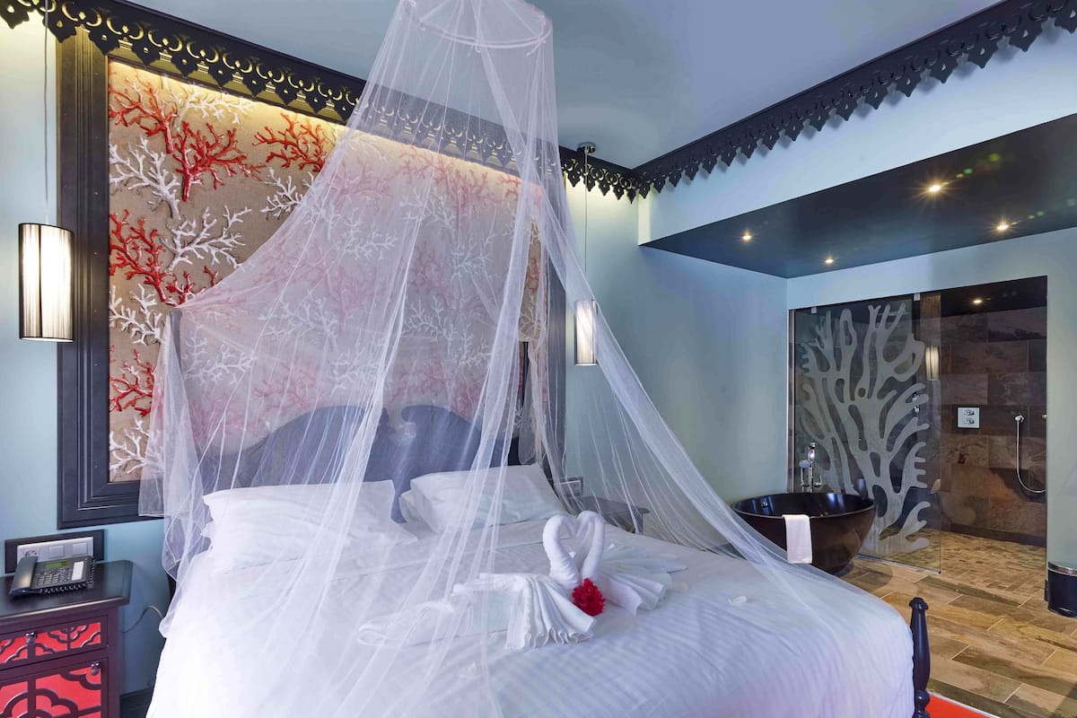 A neatly made bed with a canopy, a bedside table with a phone, and a wall with a coral coral pattern.