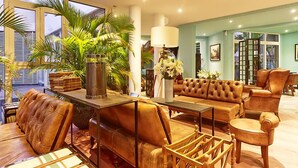 A modern living room with leather furniture, a coffee table, and a large window with a view of palm trees. - Villa Delisle Hôtel & Spa (Saint-Pierre)