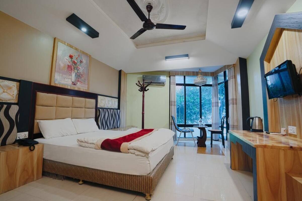 A bedroom with a bed, a desk, a chair, a television, and a window.