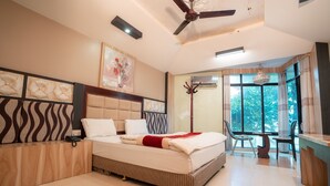 A hotel room with a large bed, a ceiling fan, a window with a view, a desk, and a chair. - Hotel Welcome (Janakpur)