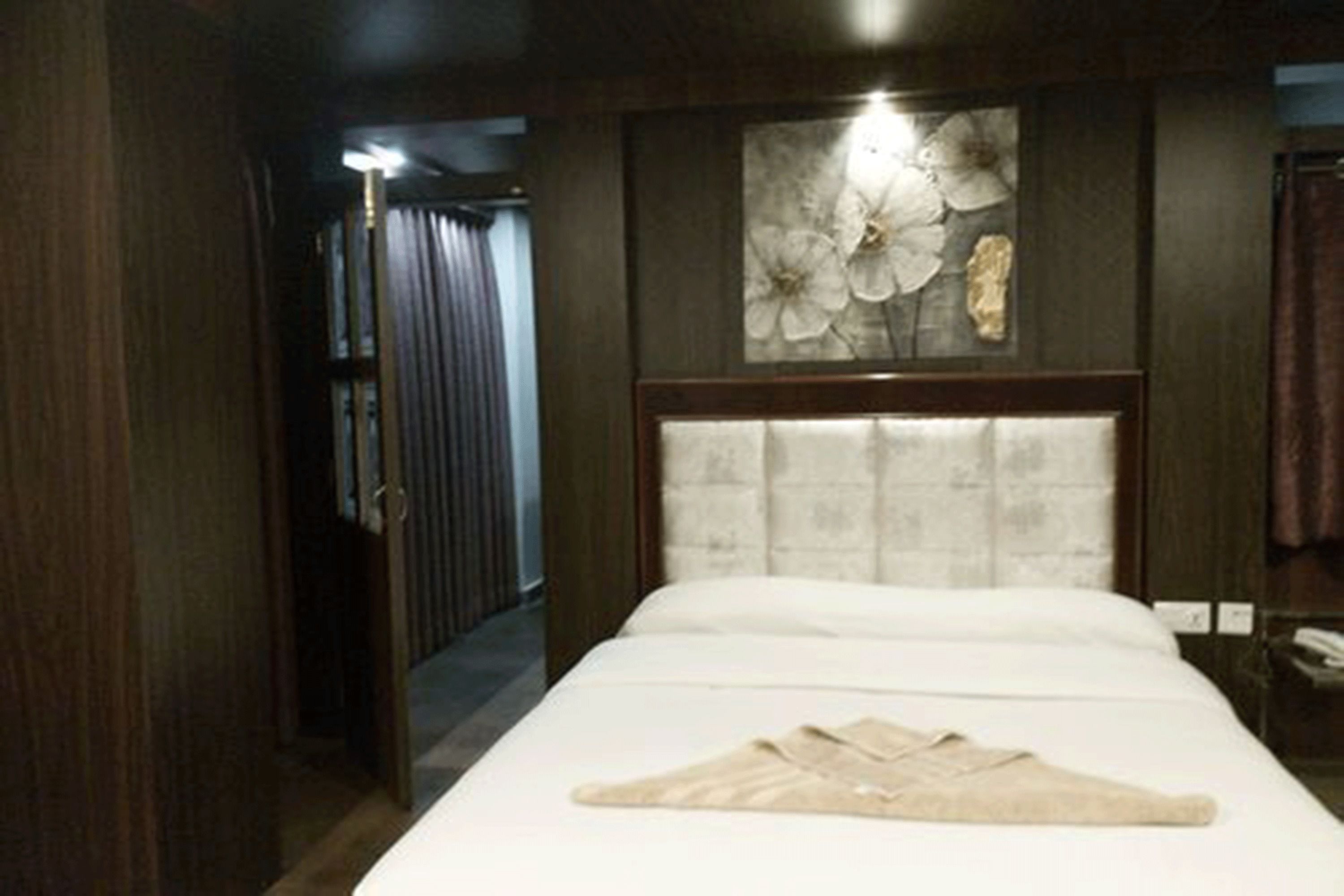 Habitación de hotel con cama, cabecero, una obra de arte colgada en la pared y una puerta que da a otra habitación.
