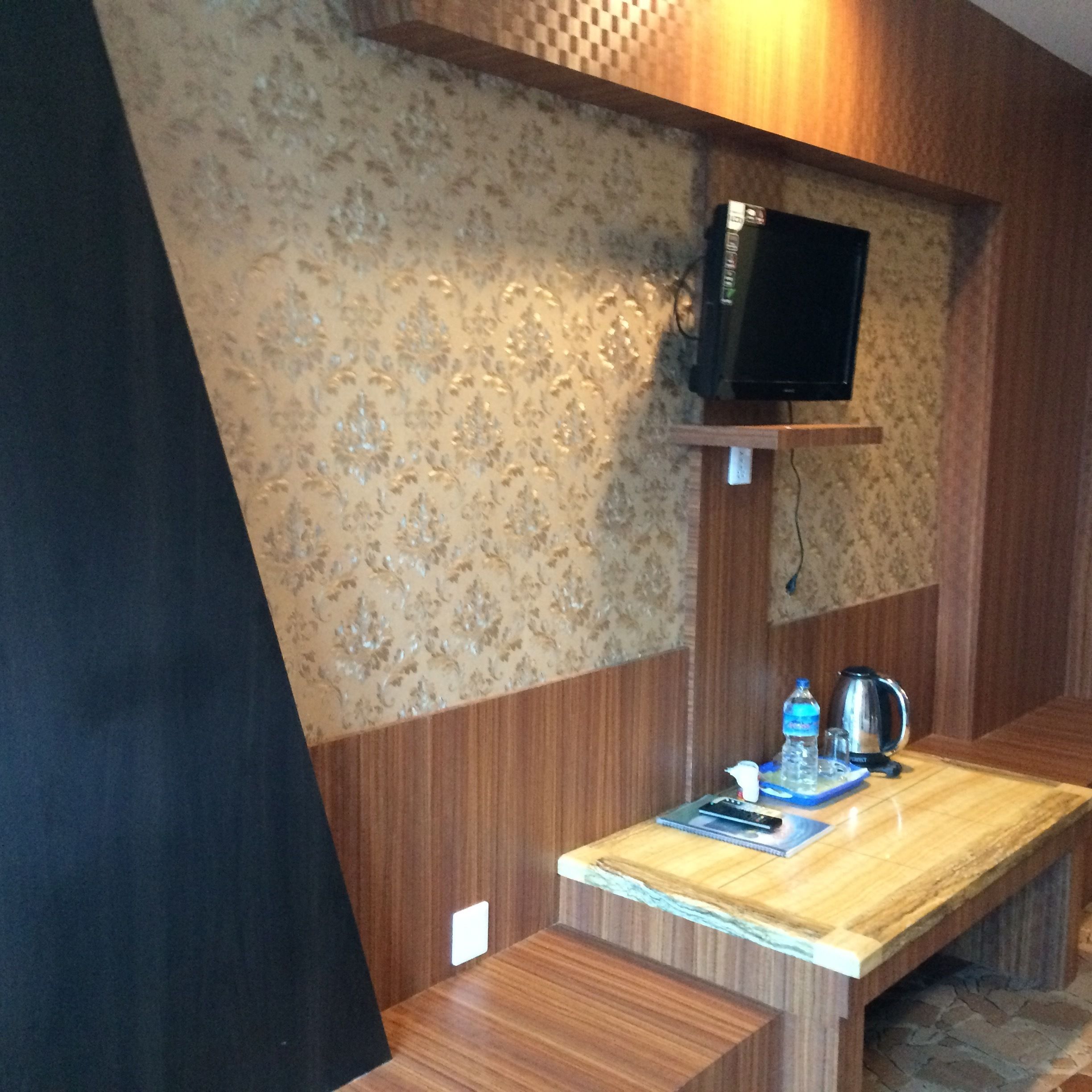 A wooden bench with a small table, a television mounted on the wall, and a water bottle on the table.