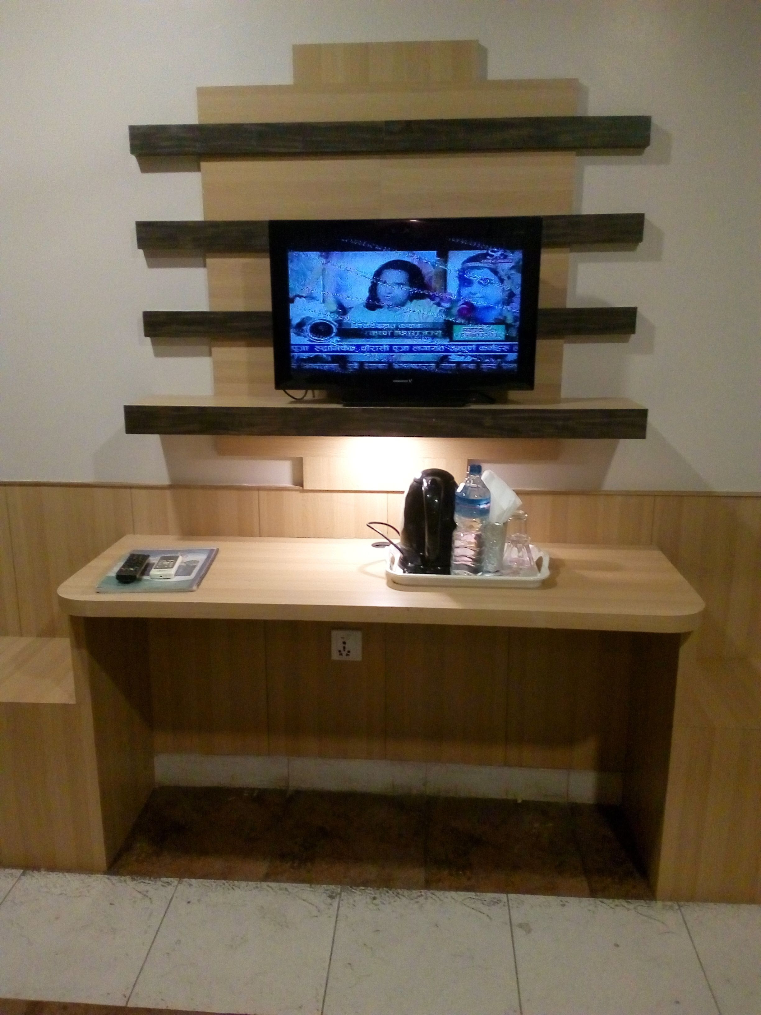 A television mounted on a wooden wall with a wooden shelf below it.