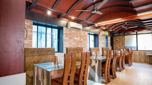 A restaurant with brick walls, wooden ceiling beams, and a long table with chairs. - Hotel Welcome (Janakpur)