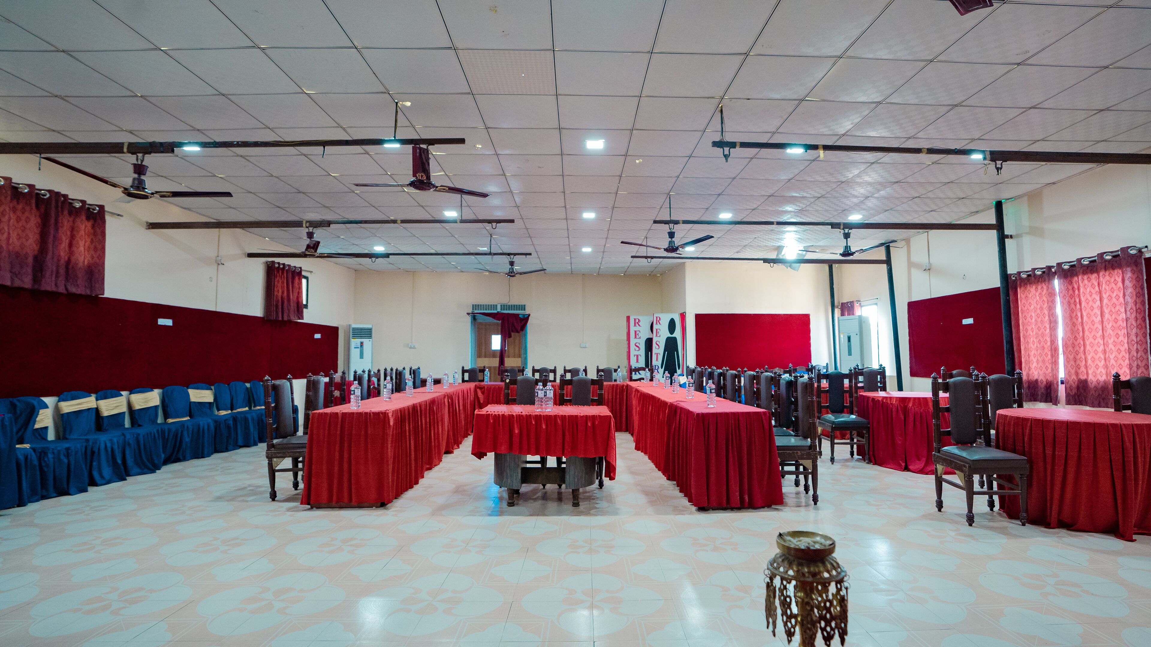 A large conference room with multiple tables covered in red tablecloths, arranged in rows.