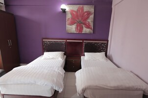 A room with two beds, a wardrobe, and a wall-mounted lamp.