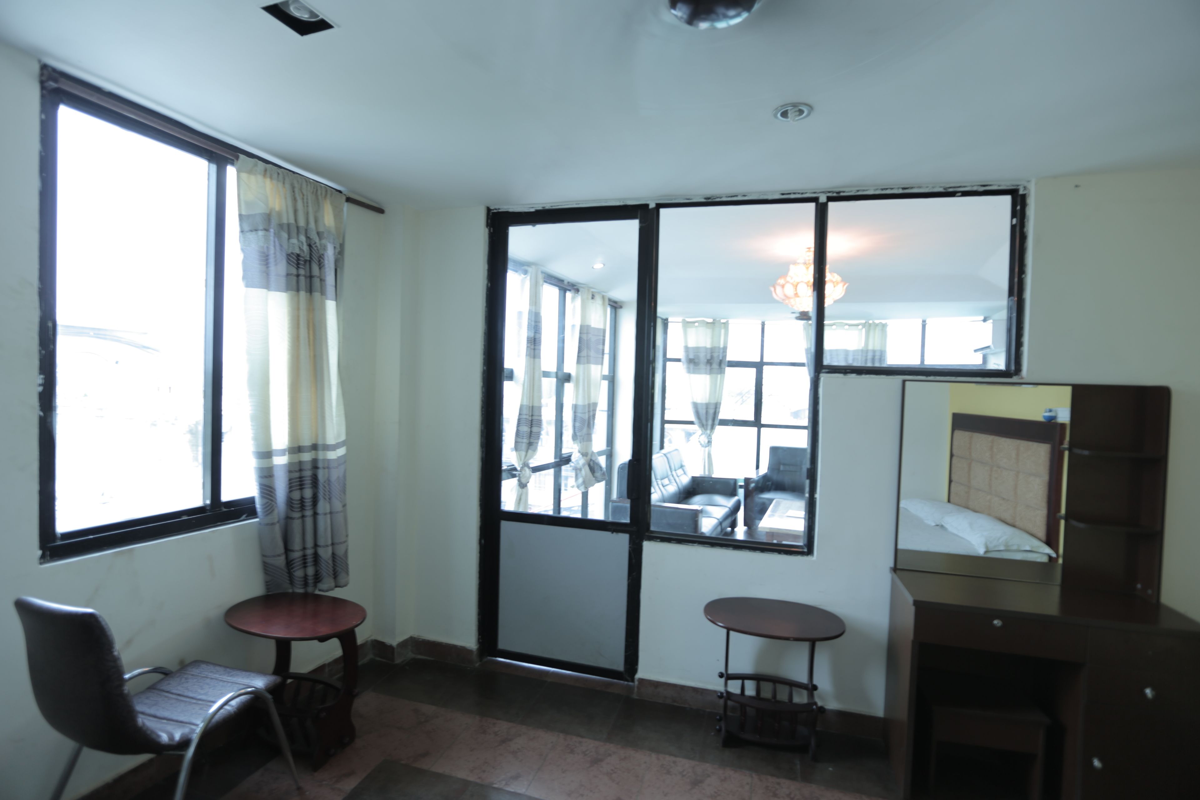 A room with a large window, a chair, a small table, a bed, and a mirror.