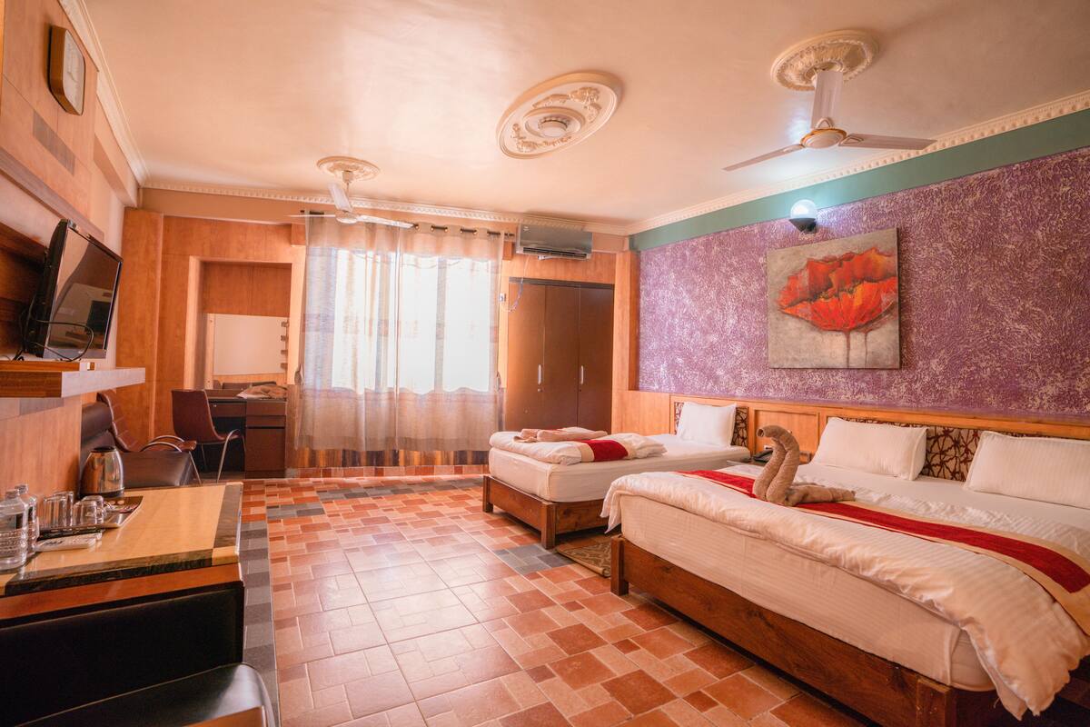 A hotel room with two beds, a desk with a chair, a television, and a large window with curtains.