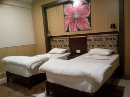 A hotel room with two single beds, a large floral artwork on the wall, and a patterned headboard.