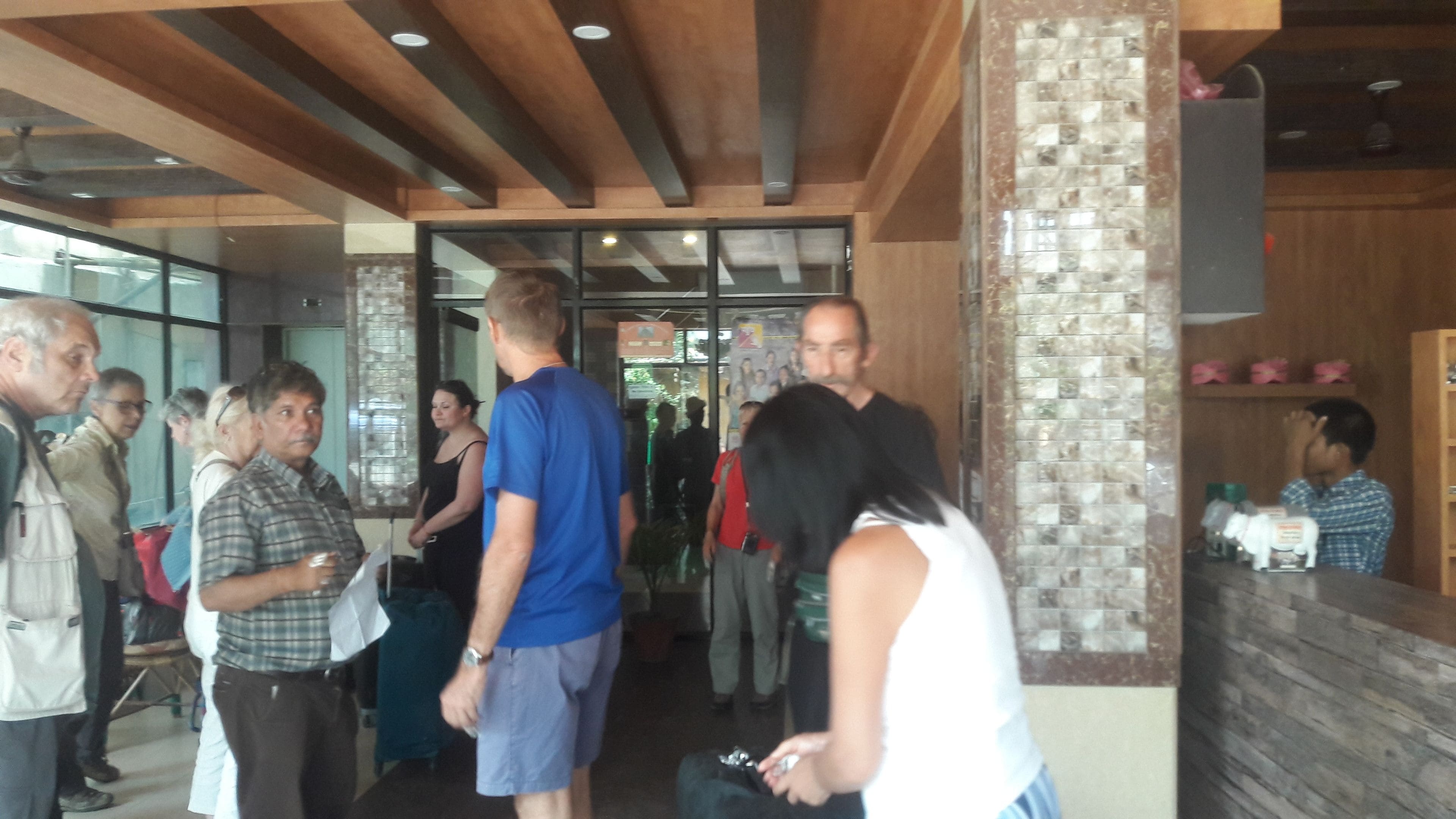 A group of people standing in a hallway with wooden beams on the ceiling and a glass door leading to another area.