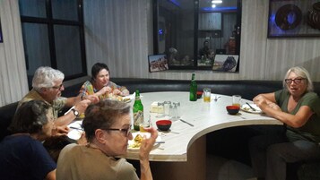 A group of people dining around a curved table in a room with a large window and wall-mounted artwork.