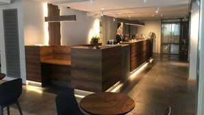 Un área de recepción moderna con un mostrador de madera, una zona de estar con una mesa redonda, y un ventanal que proporciona luz natural.