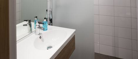 Un baño moderno con lavamanos, espejo y ducha blancos.