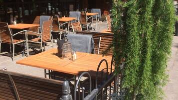 An outdoor seating area with wooden tables and metal chairs, a potted plant with white flowers, and a sign that reads "Park Bar".