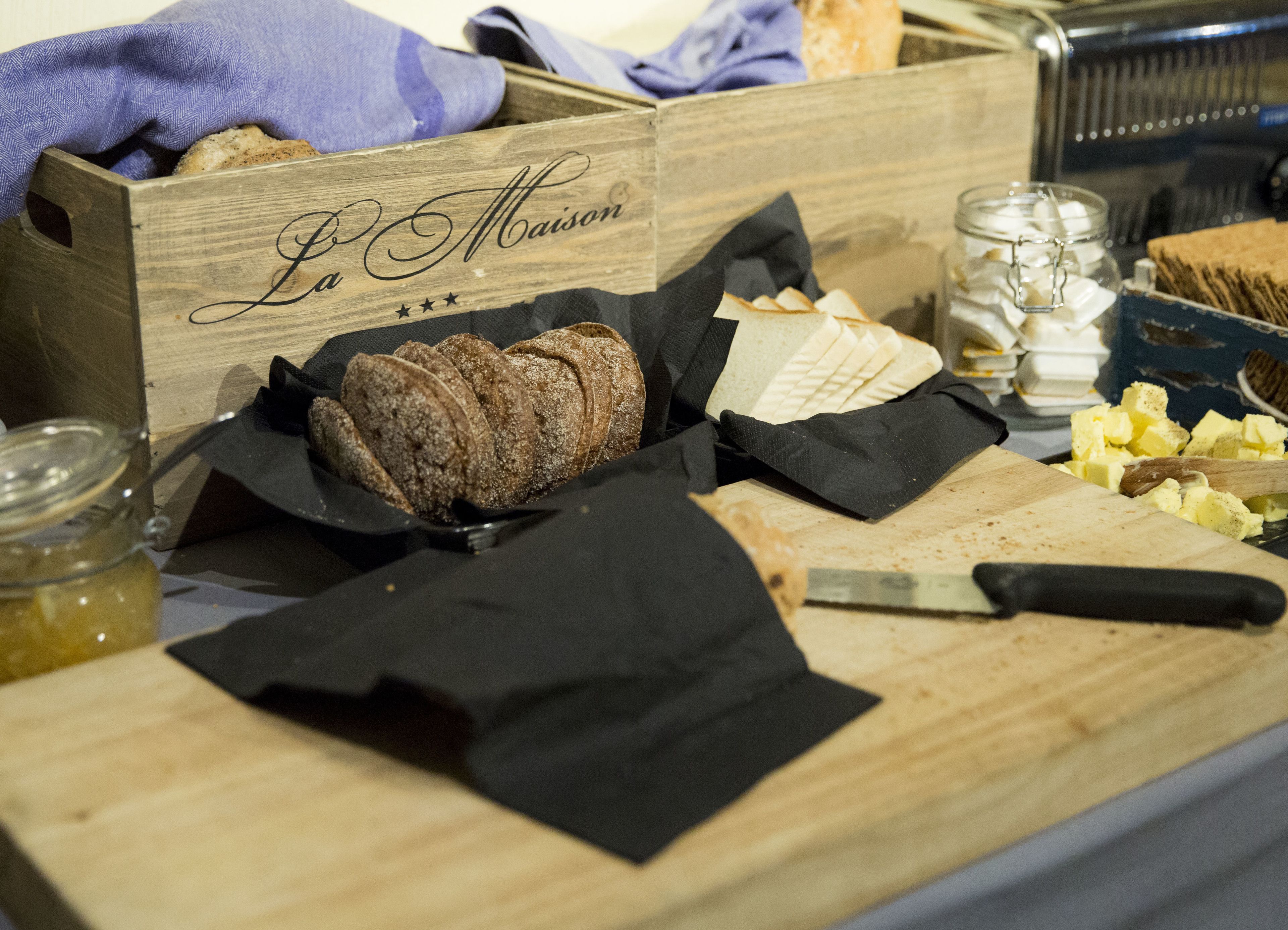 A wooden box labeled "La Maison" with sliced bread and cheese on a table.