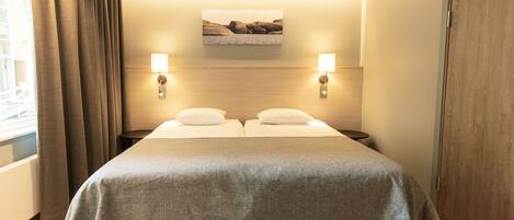Habitación de hotel con cama doble, dos lámparas de noche, un cuadro colgado en la pared y un armario de madera.