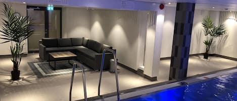 A modern indoor pool area with a sectional sofa and potted plants.