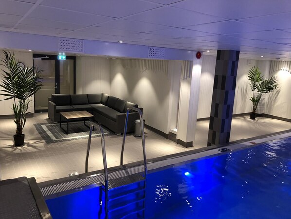 A modern indoor pool area with a sectional sofa and potted plants. - Park Alandia Hotel (Mariehamn)