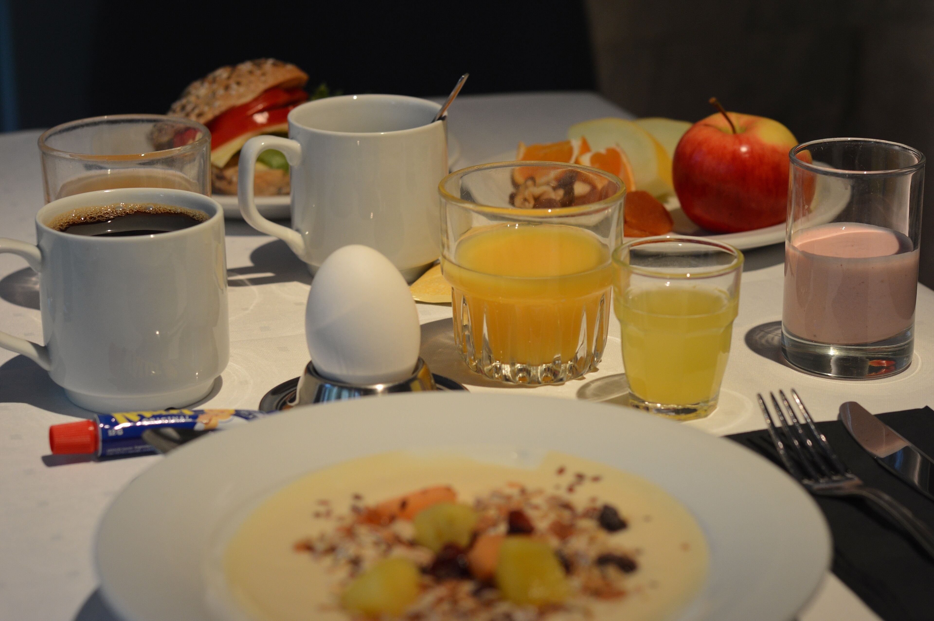 A breakfast table with various food items and drinks, including a plate of soup, a sandwich, and a glass of orange juice.