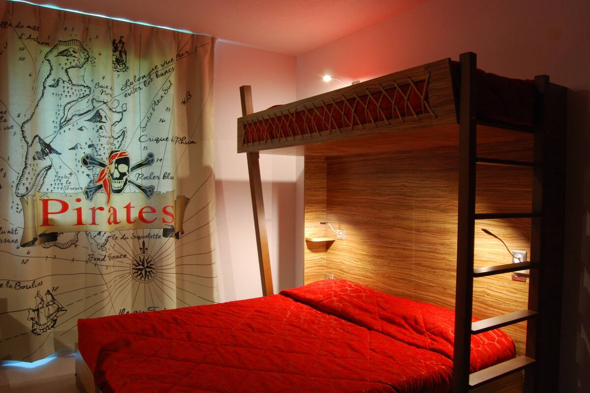 Een stapelbed met een rode dekbedovertrek en een wereldkaart met piratenthema.