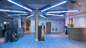 Un lobby moderno con una columna central, mostrador de recepción de madera y una estatua.