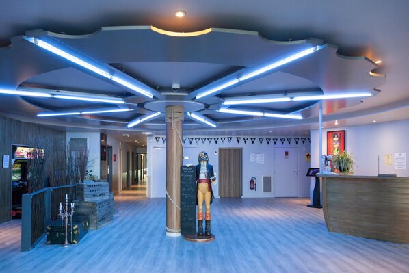 A modern lobby with a central column, wooden reception desk, and a statue.