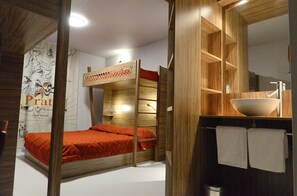 Een stapelbed met een rode matras, houten hoofdbord en een muur met een poster. Er is een houten plank met een wastafel en een spiegel erboven.