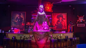 Zona de bar con una escultura de hielo central que dice 'Piratas', rodeada de taburetes y estantes con botellas.