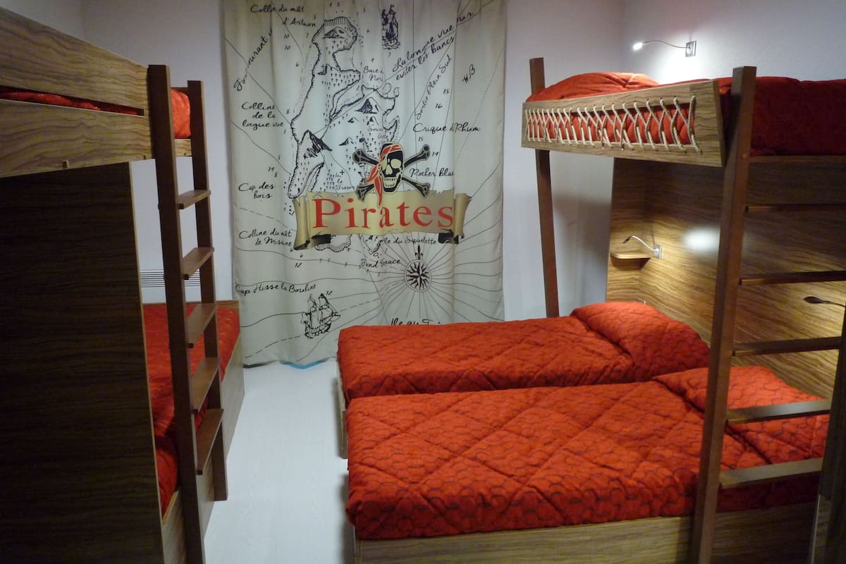 Een slaapkamer met stapelbed, gordijn met een wereldkaartmotief, een houten ladder en een rode, gewatteerde sprei.