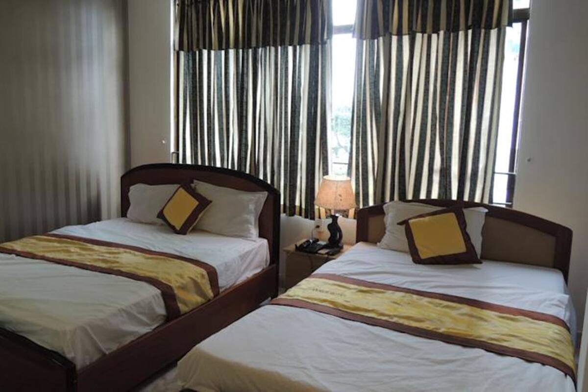 Habitación de hotel con dos camas individuales, una mesita de noche con lámpara y una ventana con cortinas a rayas.