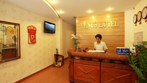 A reception desk at Venus Hotel with a wooden finish, a television above it, and a sign indicating the reception area. - Venus Hotel (Nha Trang)