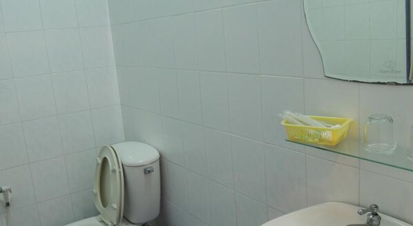 Un baño con azulejos blancos, un inodoro, un estante de cristal con una cesta amarilla y un lavabo.
