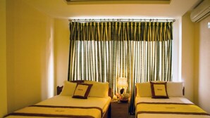 A hotel room with two beds, a nightstand with a lamp, and a window with striped curtains. - Venus Hotel (Nha Trang)