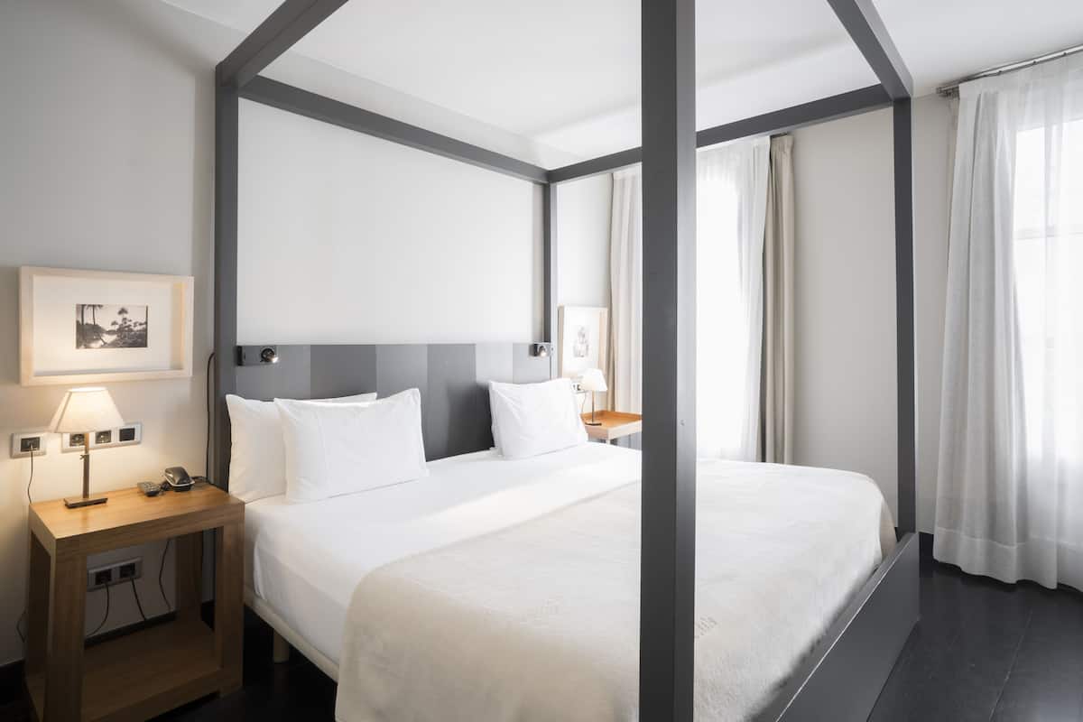 Quarto de hotel moderno com uma cama grande, mesas de cabeceira de madeira e painel de cabeceira.