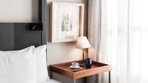 A hotel room with a bed, a bedside table with a lamp, a framed picture, and a window with curtains. - Banys Orientals (Barcelona)