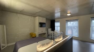 A modern bedroom with a bed, a TV mounted on the wall, and large windows.