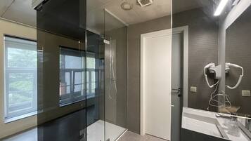 Un baño moderno con cabina de ducha de vidrio, un lavamanos blanco y un espejo con secador de pelo.