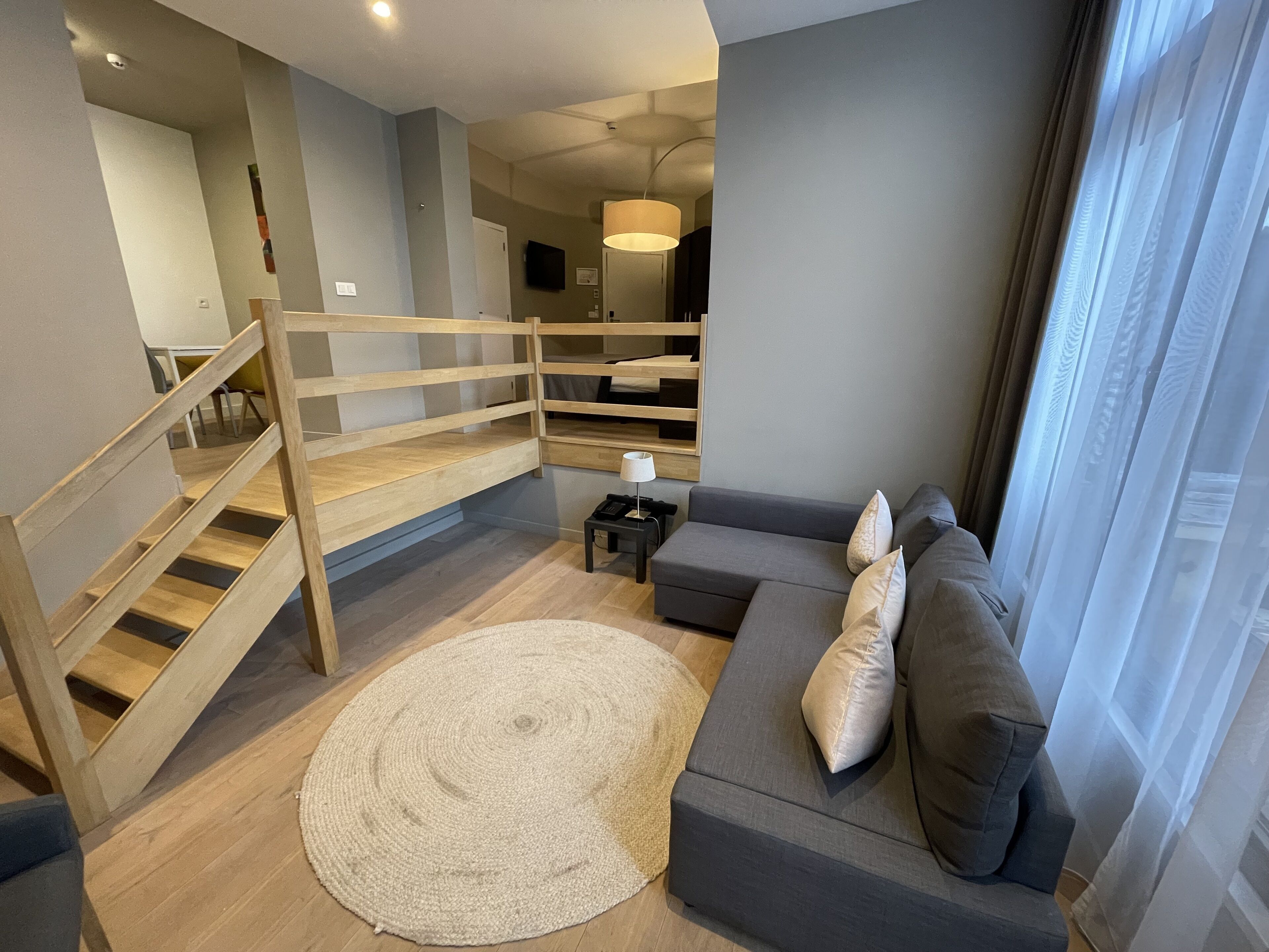 A modern living room with a grey sofa, a wooden staircase, and a round rug.