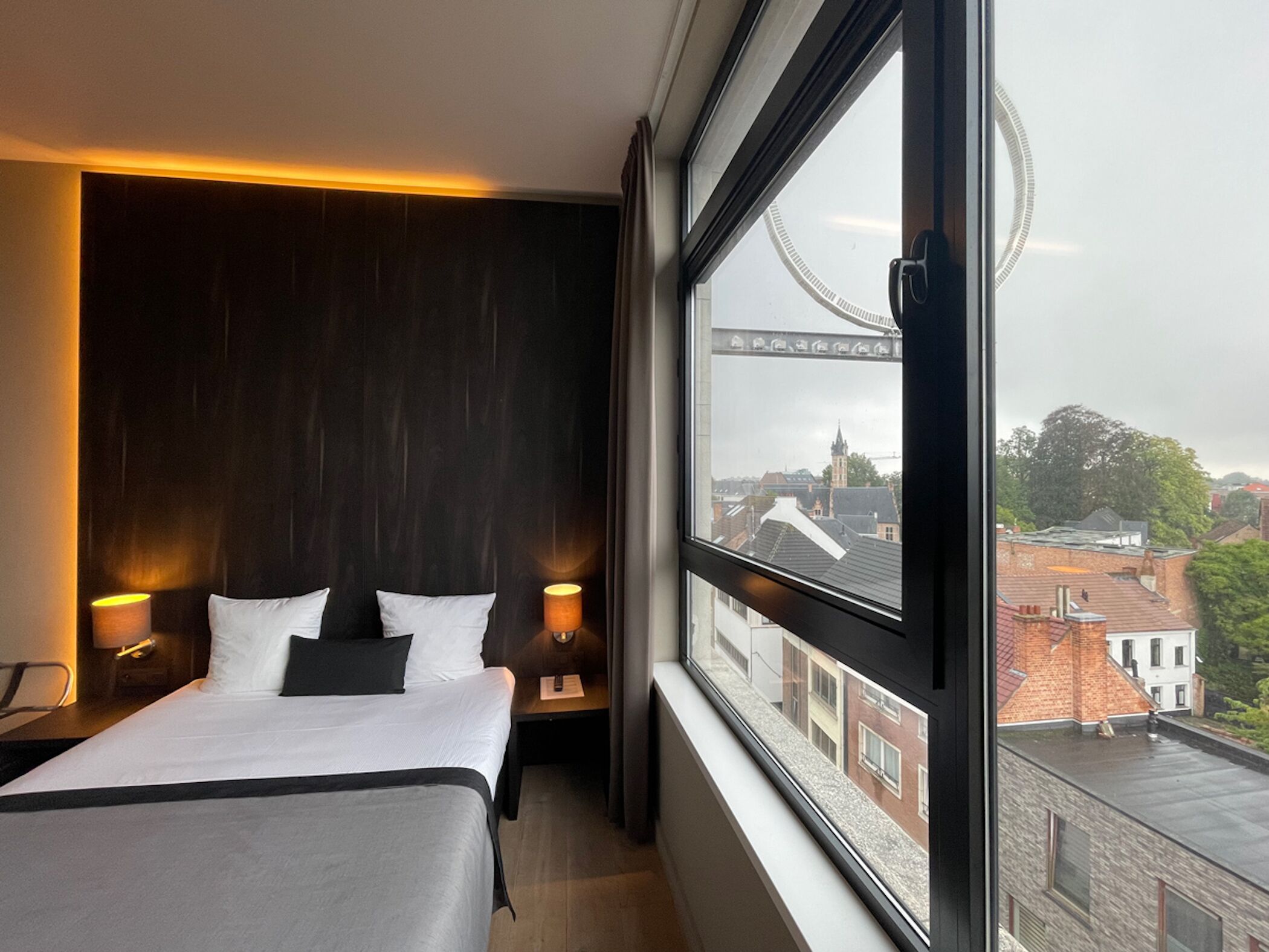 A hotel room with a large bed, two bedside tables, a window with a view of buildings and a bridge.
