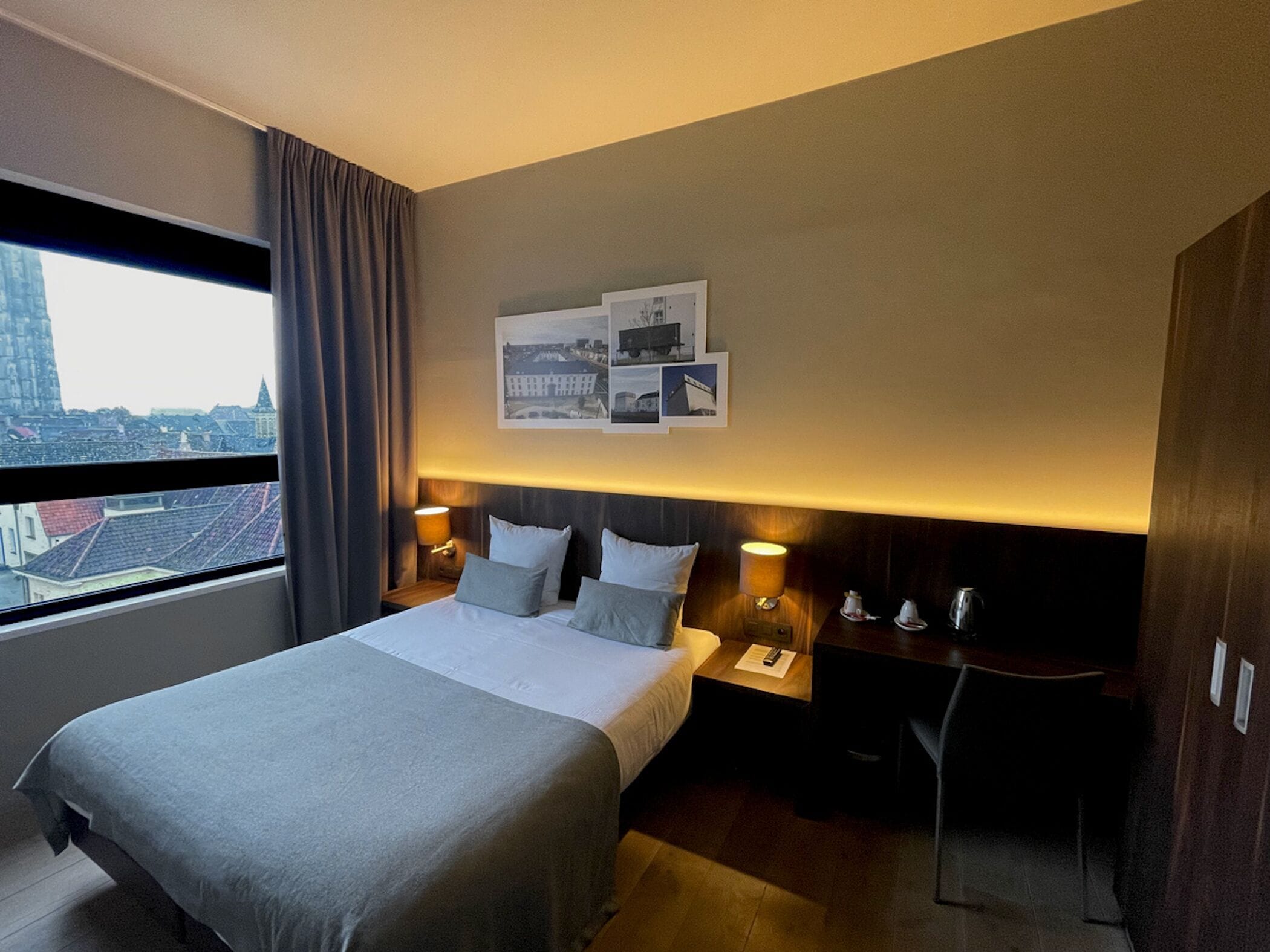 A hotel room with a bed, bedside tables, a desk, and a city view.