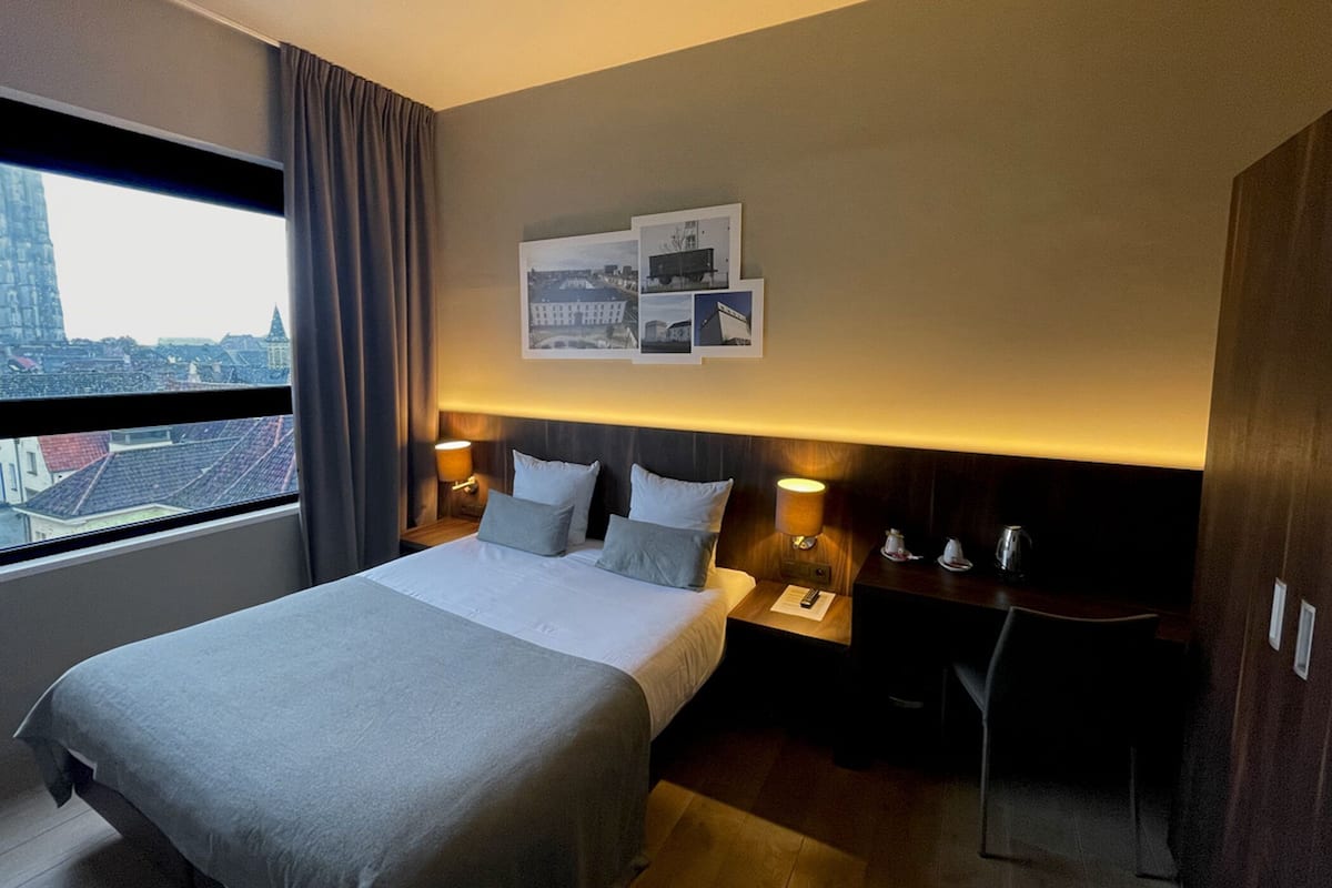 A hotel room with a bed, bedside tables, a desk, and a city view.