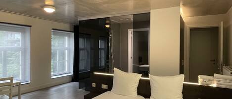 A modern hotel room with a large bed, a seating area, and a view of the outdoors.