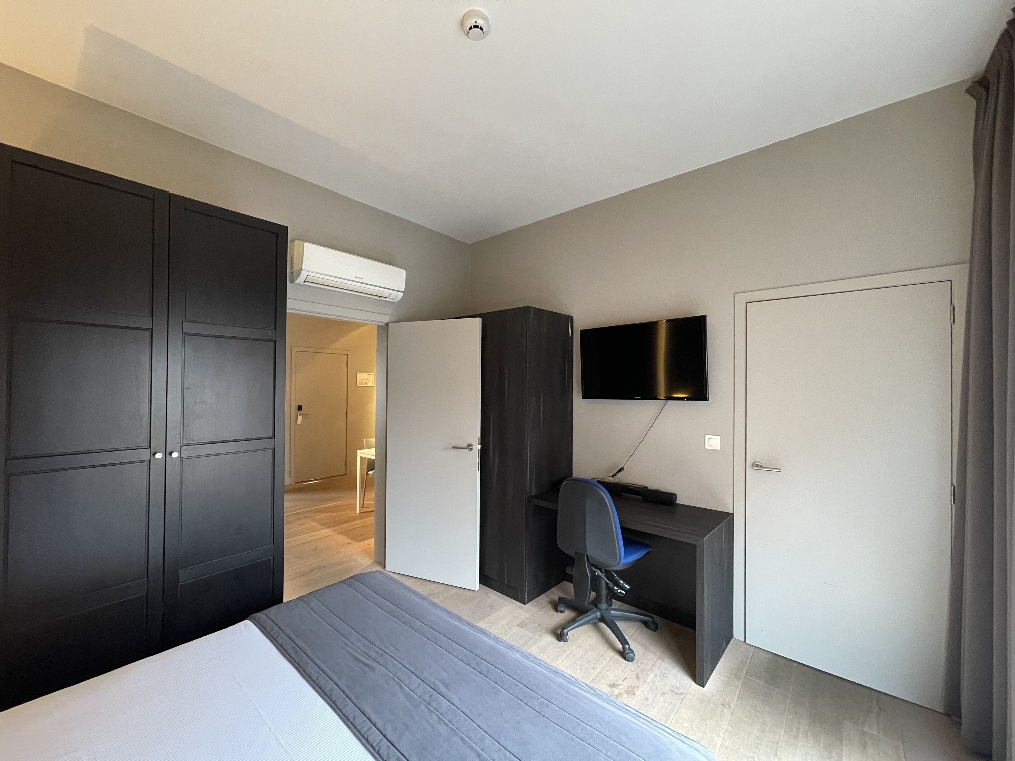 Une chambre d’hôtel comprenant un lit, un bureau avec une chaise, un téléviseur fixé au mur et une armoire.