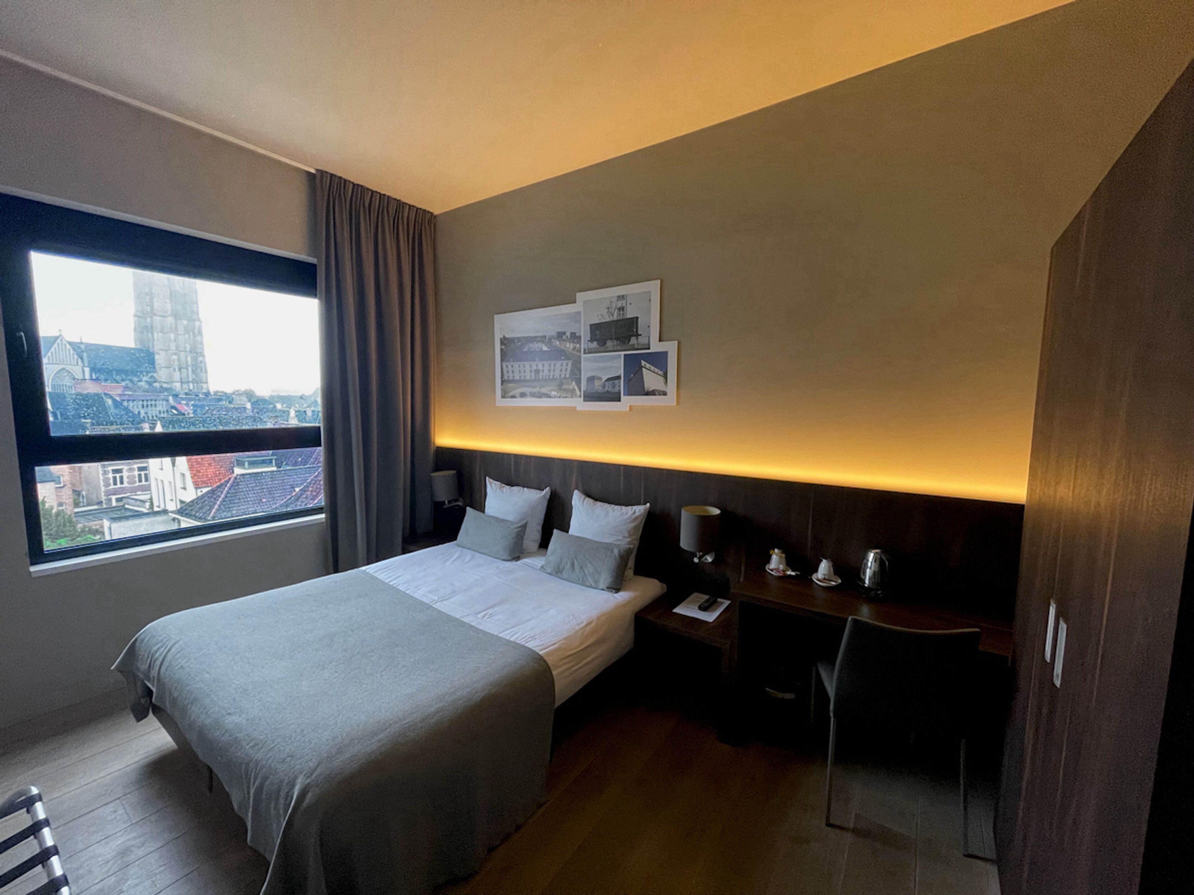Een hotelkamer met een groot bed, een bureau, een stoel, een nachtkastje en een raam met uitzicht over de stad.