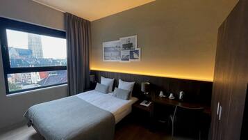 Een hotelkamer met een groot bed, een bureau, een stoel, een nachtkastje en een raam met uitzicht over de stad.