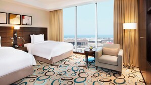 Habitación de hotel con dos camas, un sofá, un ventanal grande con vista a la ciudad y una alfombra estampada.