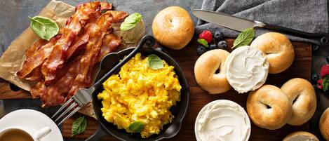 A breakfast setting with bacon, scrambled eggs, bagels, and fresh berries.